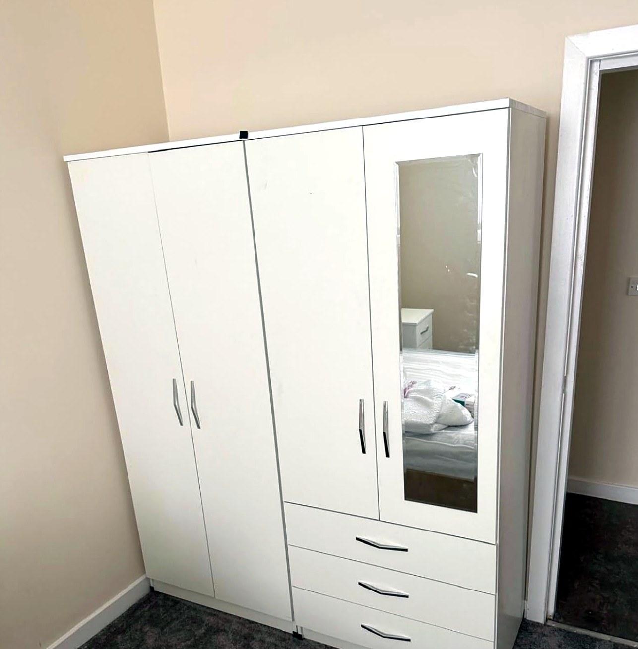 White four-door wardrobe with a mirror door and three drawers, assembled