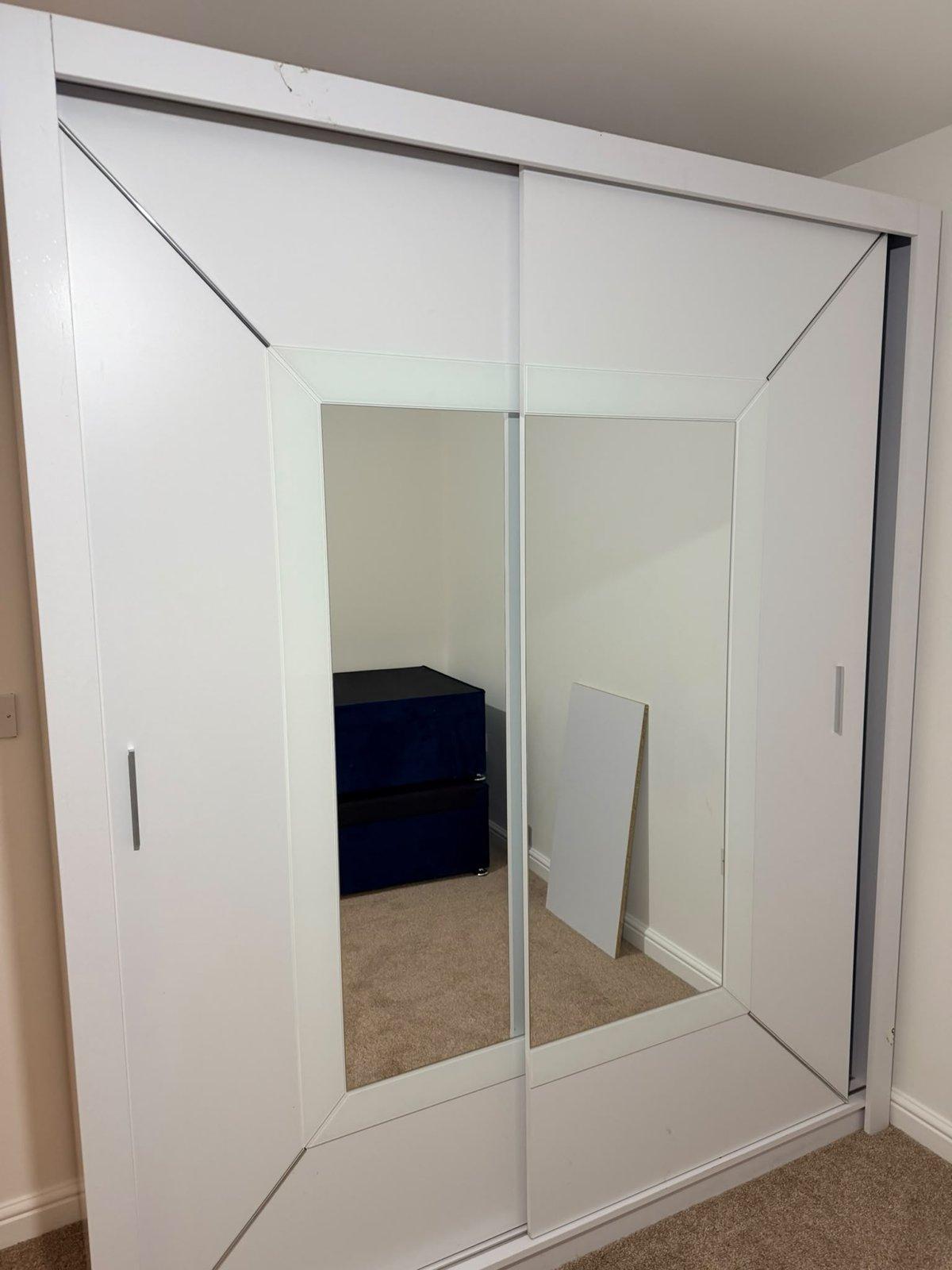 White sliding-door wardrobe with full-height mirror panels, assembled in a bedroom