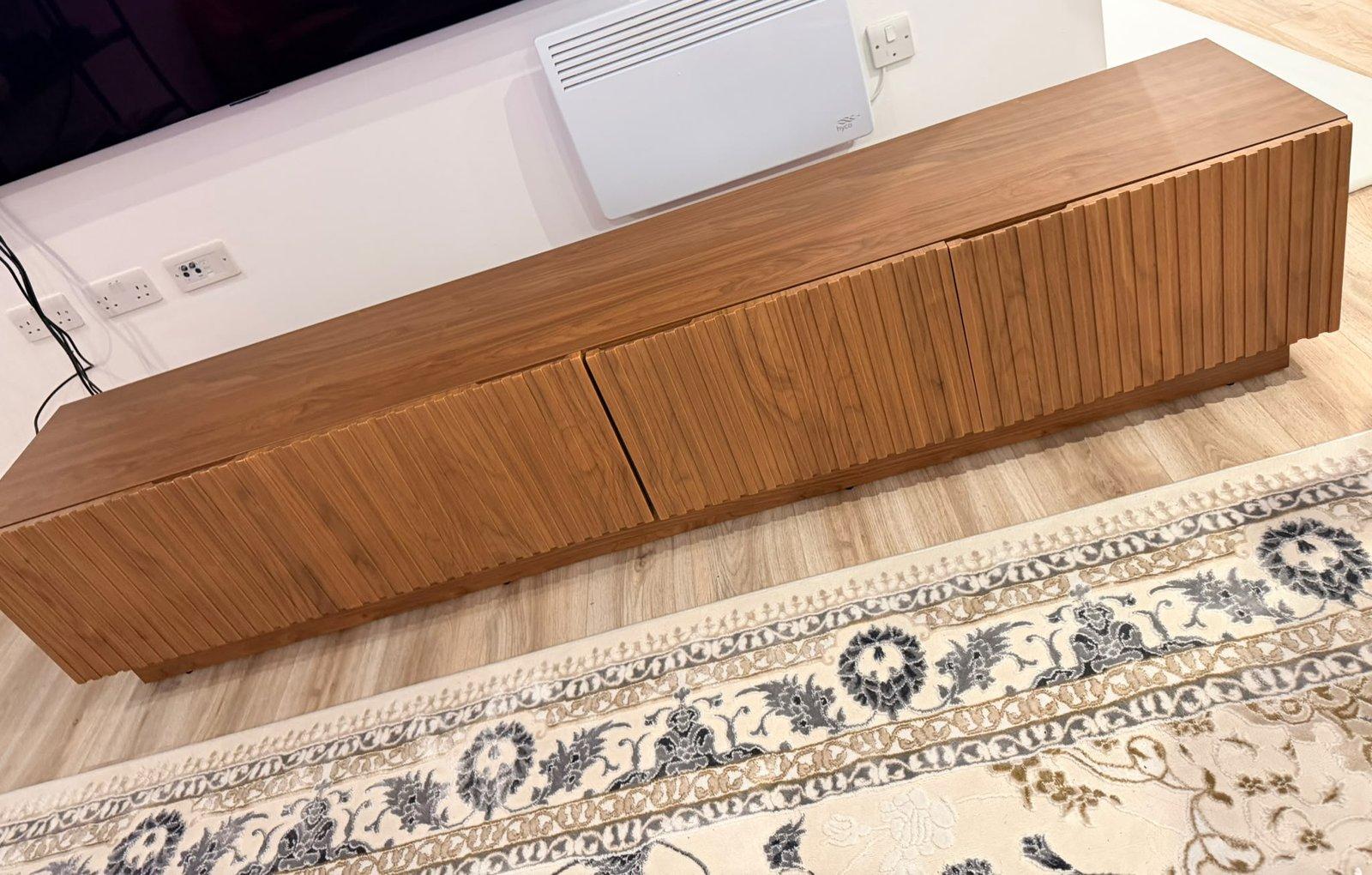 Long walnut-effect TV unit with fluted doors, assembled under a wall-mounted TV