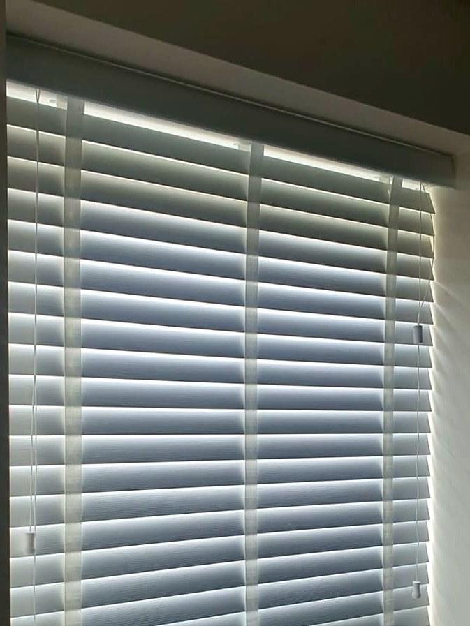 White faux wood venetian blind fitted in a kitchen window, slats tilted half open