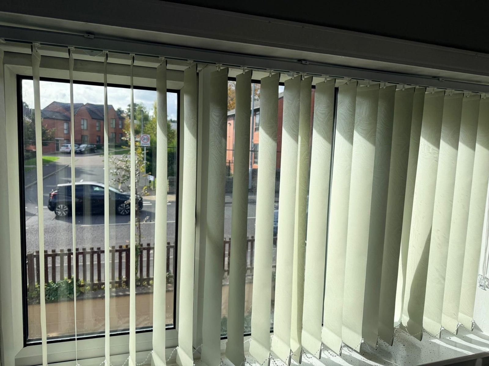 Cream vertical blinds across a wide front window, louvres half open onto the street