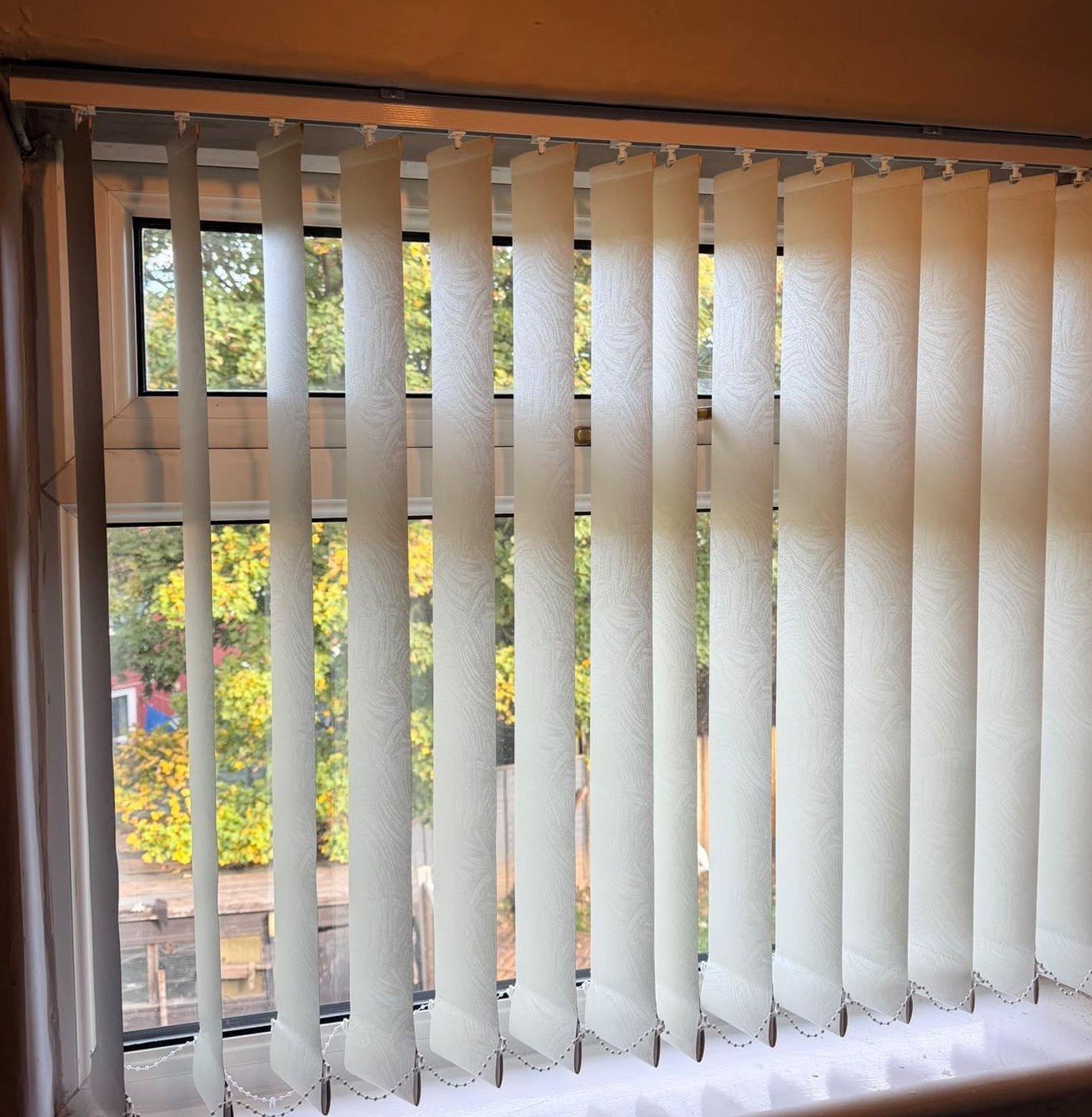 Cream vertical blinds in a bedroom window recess, louvres turned to the garden
