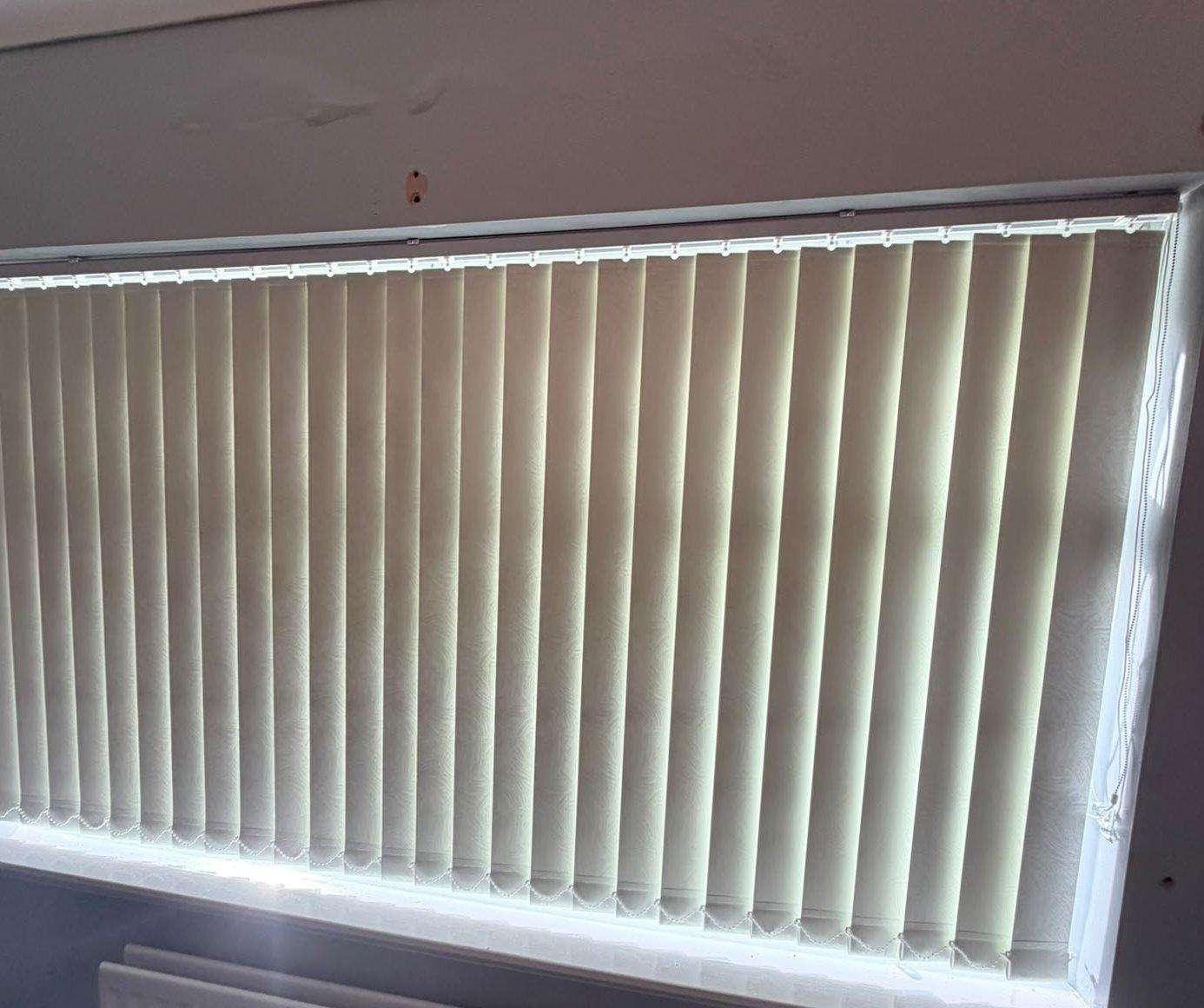 Cream vertical blinds closed across a wide window above a radiator