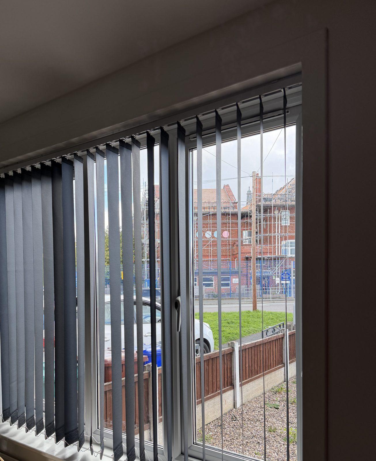 Grey vertical blinds fitted inside a front room window recess