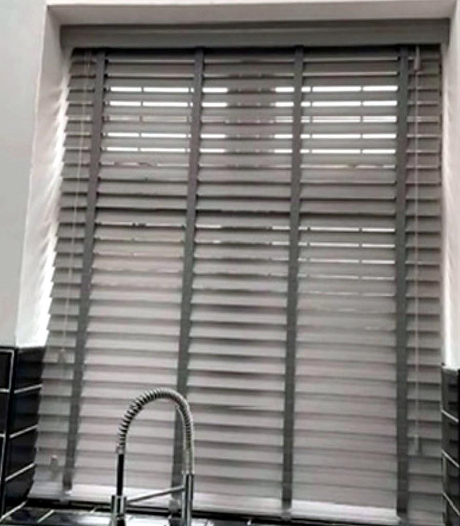 Grey wood venetian blind with tapes, fitted in a kitchen window above the sink