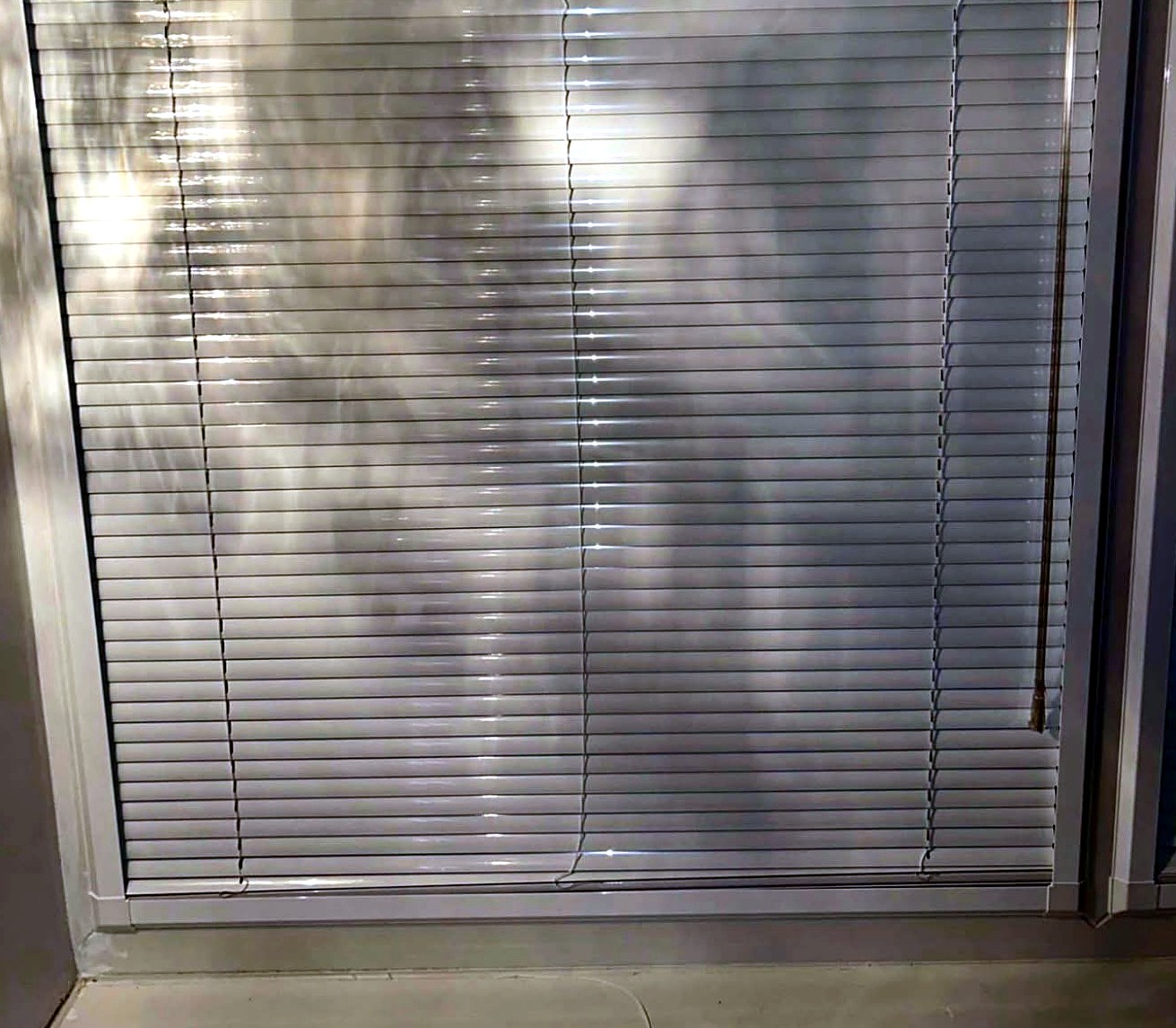 Silver aluminium venetian blind fitted to a window, slats closed