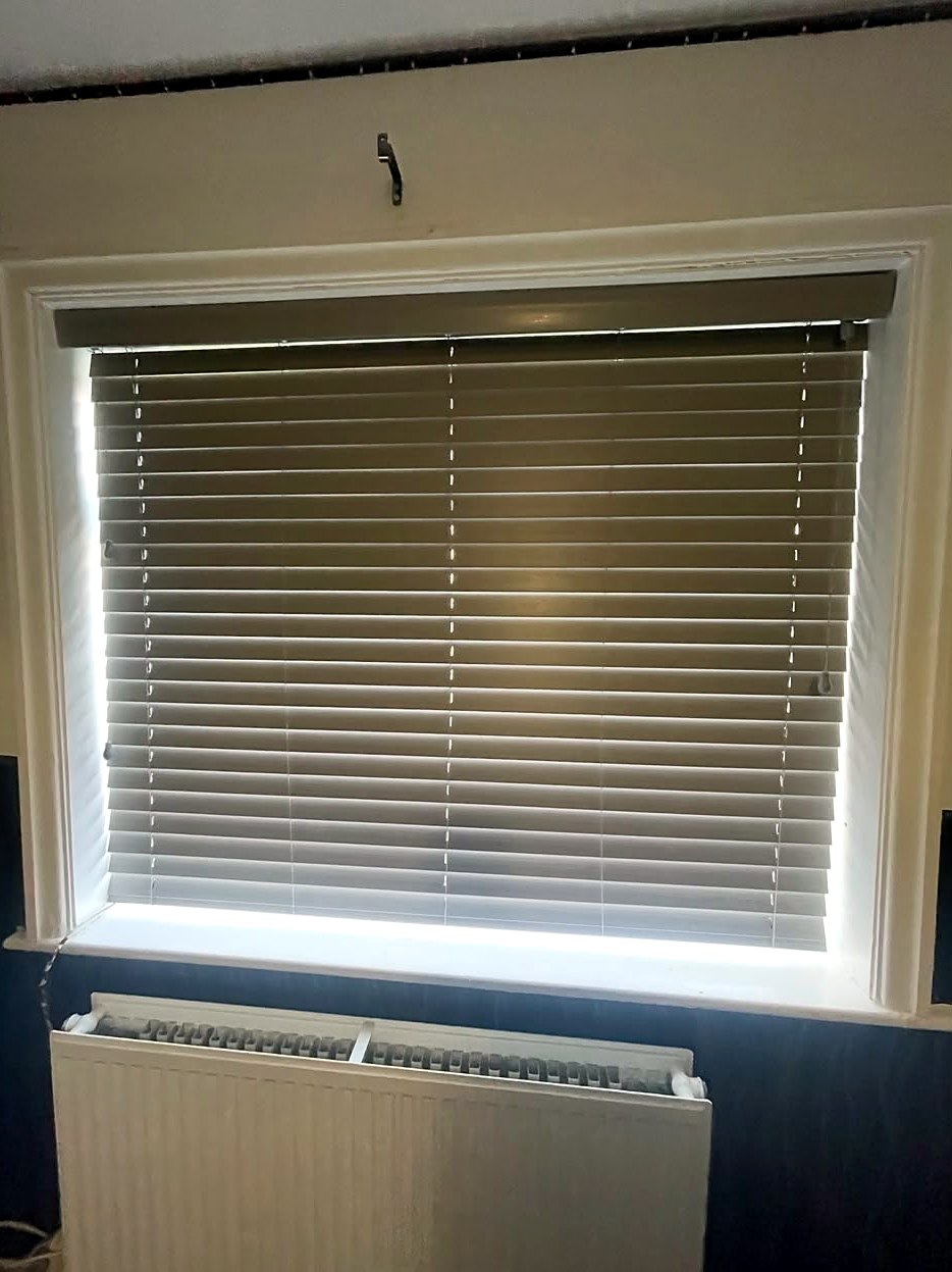 Grey faux wood venetian blind fitted inside a bedroom window recess, above a radiator