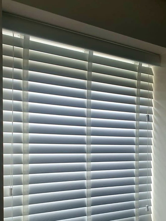 White faux wood venetian blind fitted in a kitchen window, slats tilted half open