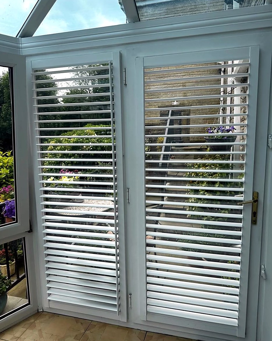 White shutters fitted to a conservatory door, louvres open onto the garden
