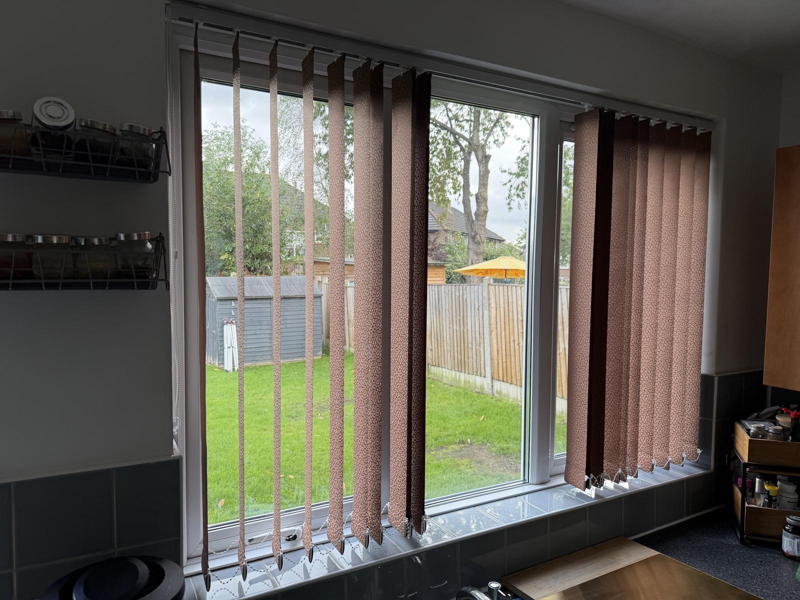 Patterned vertical blinds fitted to a wide kitchen window above a tiled worktop