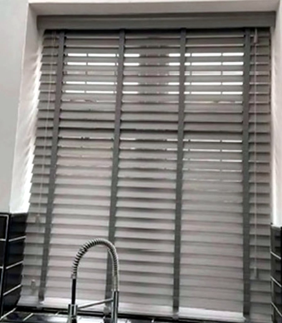 Grey wood venetian blind with tapes, fitted in a kitchen window above the sink